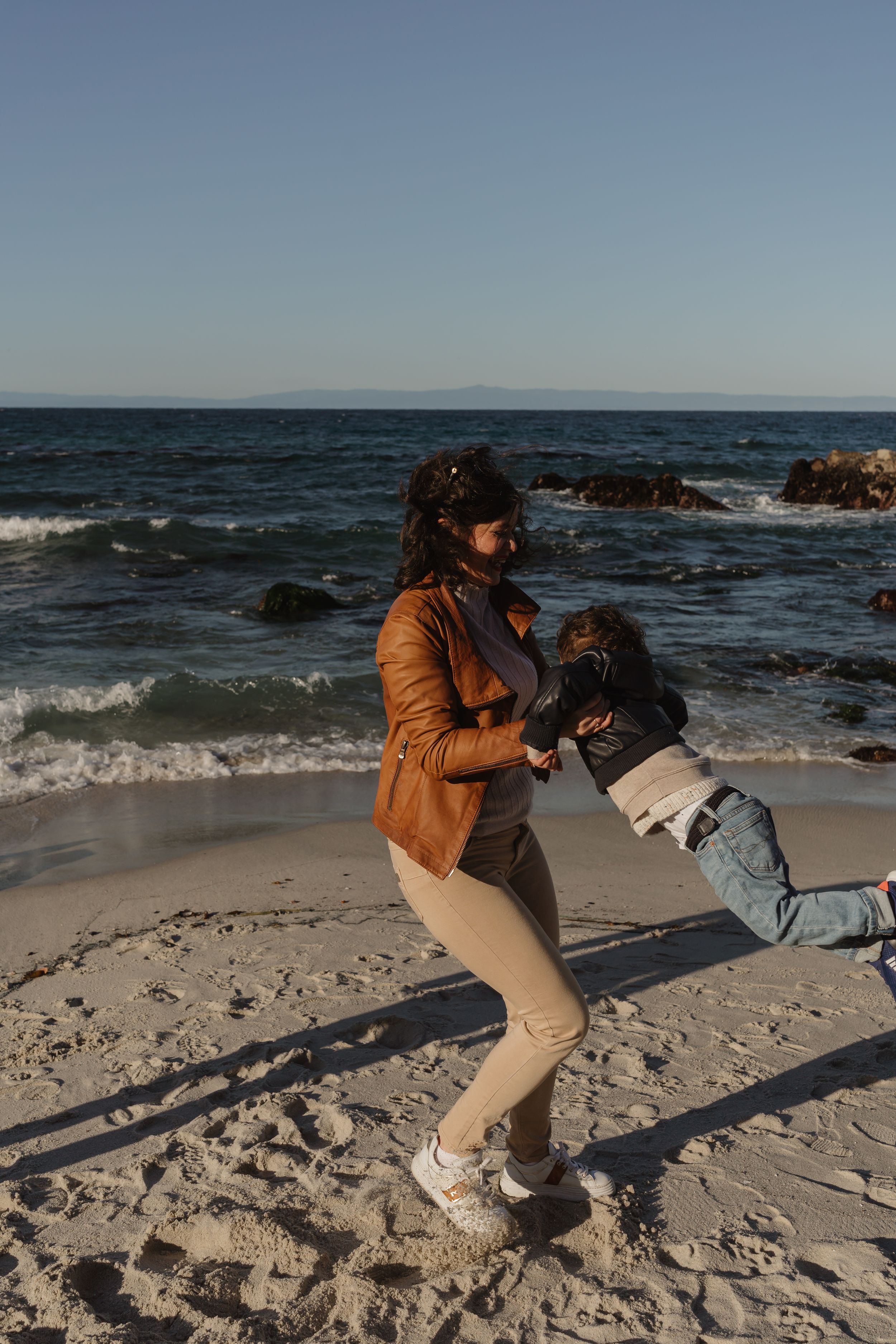 A playful moment captured at the beach during sunset with a tan leather jacket and khaki pants against the ocean waves.