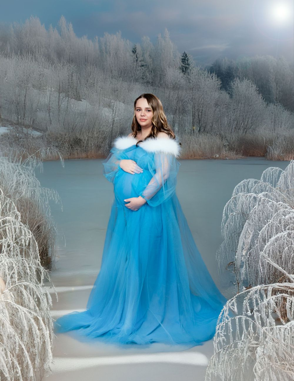 Ethereal maternity portrait in flowing blue gown amidst frosty winter landscape and misty lake.