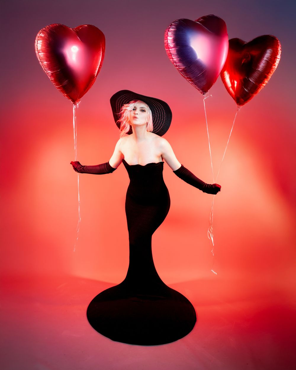 Elegant portrait of a pregnant girl in Hirwaun studio with black dress and red heart-shaped balloons against vibrant red background.