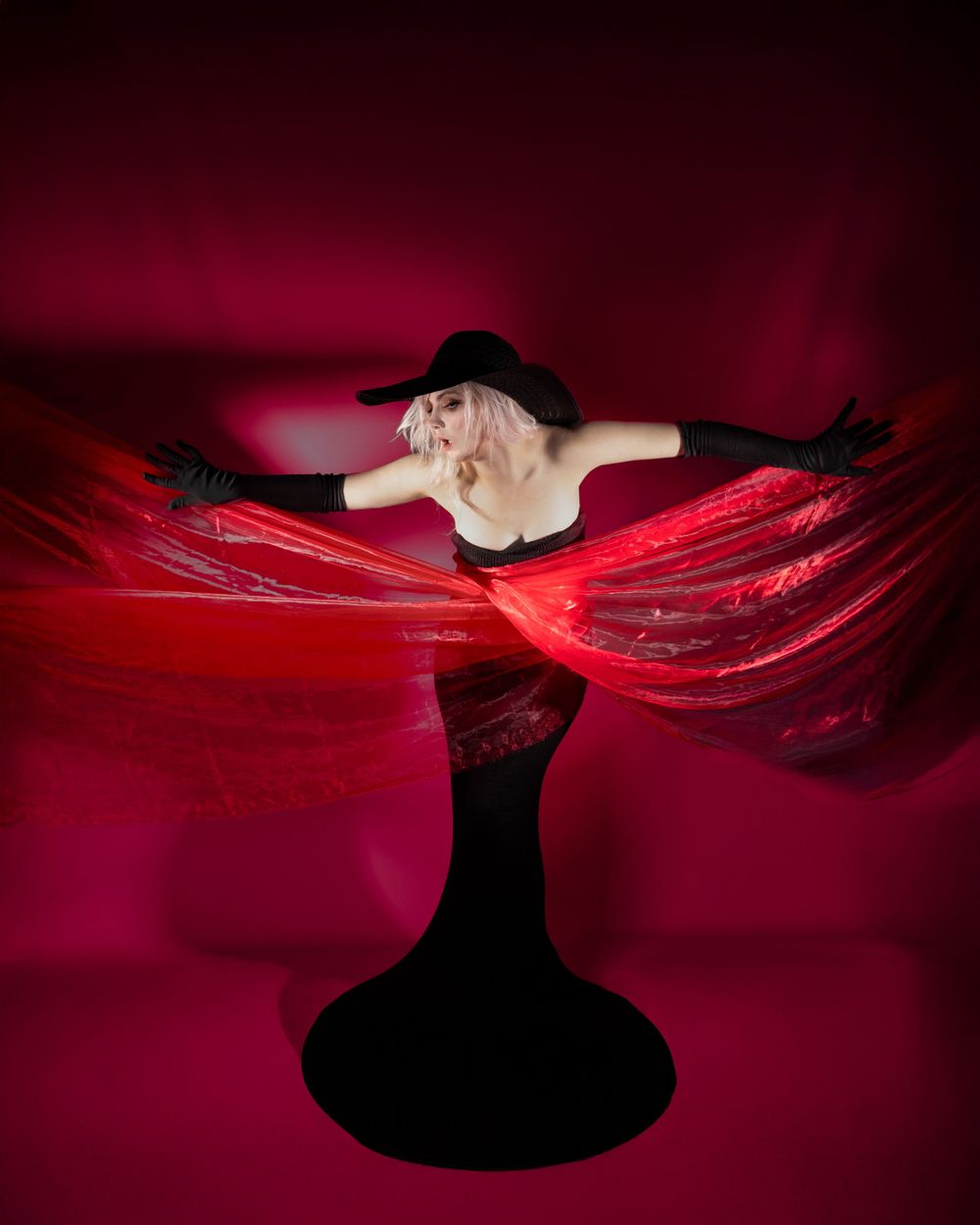 Dramatic red and black silhouette with flowing fabric against dark background.