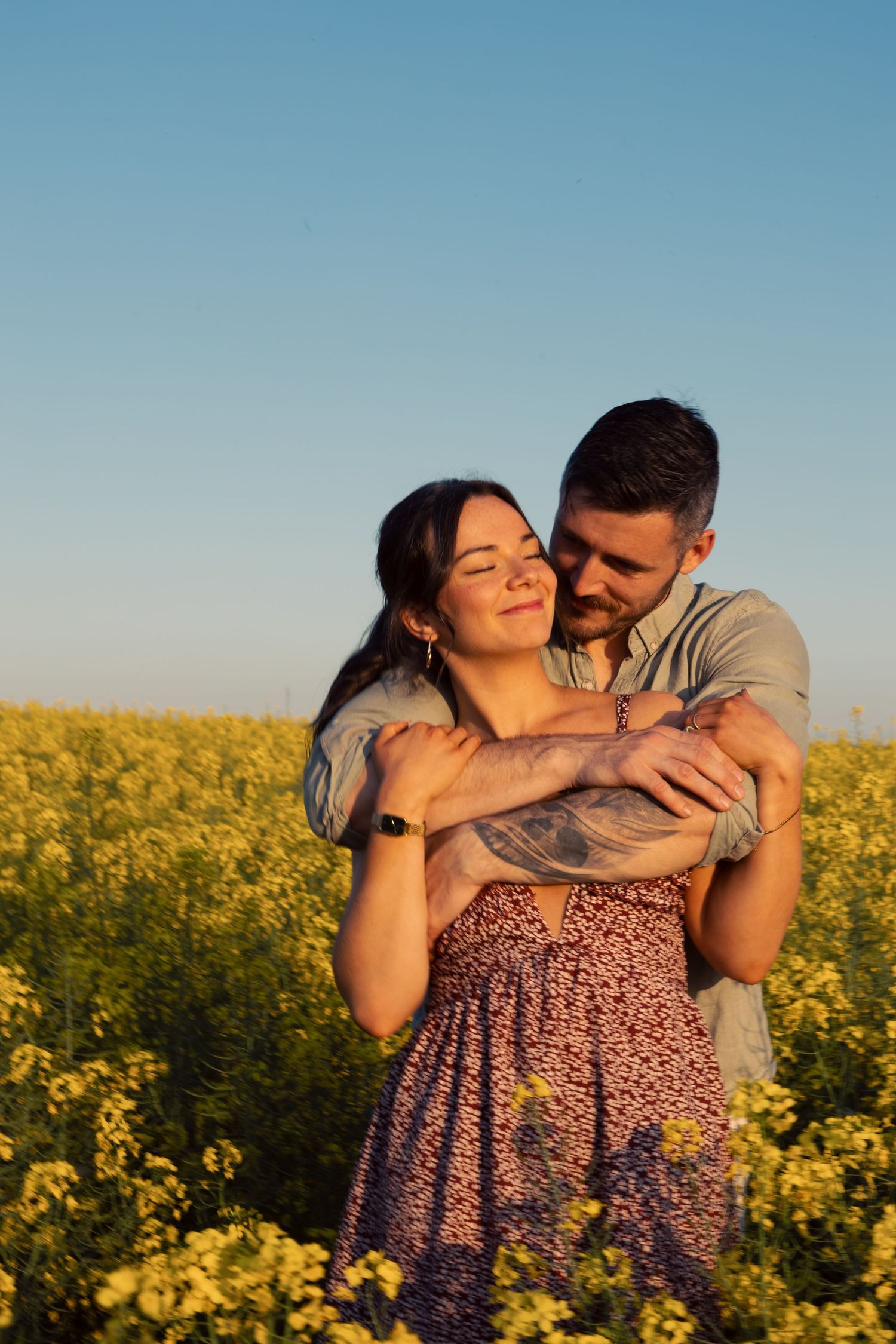 Romantic couple embraces in golden sunset light among blooming yellow canola flowers in a beautiful rural field.