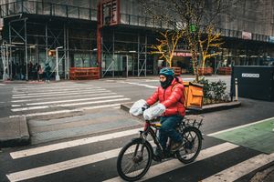 Delivery cyclist rides past urban intersection with planters and crosswalks.