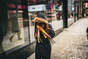 Winter street scene with snow on ground and people walking past retail shops.