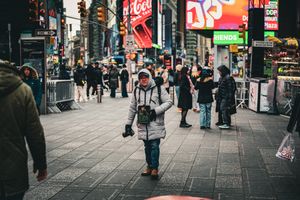 Pedestrians walk along a busy city street with bright neon signs and storefronts.