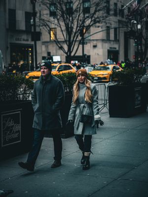 People walking on a city sidewalk with yellow taxis visible in the background.