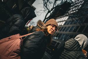 Person wearing winter clothing and knit hat walking on city street.