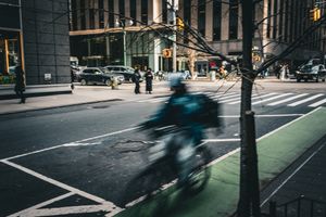 Blurred cyclist rides through urban intersection with tall buildings in background.
