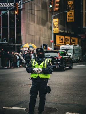 Police officer in high-visibility vest stands on duty at busy city intersection during evening hours.