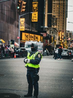 Security personnel in reflective vest monitoring a busy city intersection near Broadway theaters.