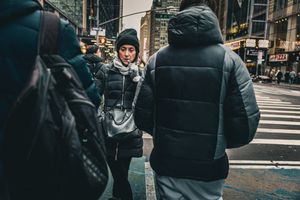 People walking on a city sidewalk wearing winter coats and backpacks.