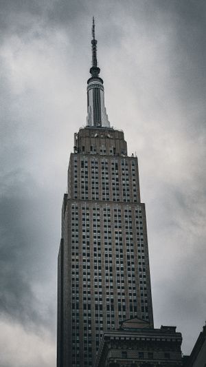 Empire State Building towers against cloudy sky in dramatic black and white shot.