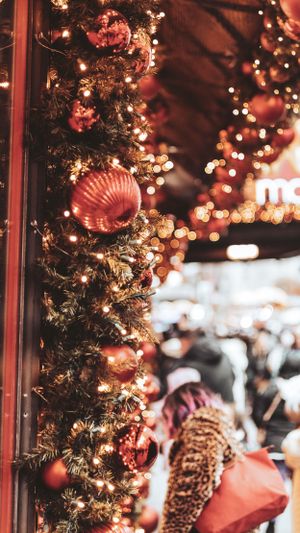 Red Christmas ornaments and garland decorate a storefront with warm glowing lights.