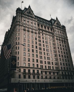 Historic Plaza Hotel facade in New York City with American flag under cloudy skies.