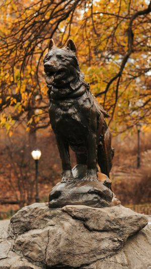Famous Balto dog statue on rock pedestal with golden autumn leaves in background.