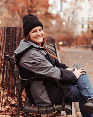 Photographer relaxing near Central Park statue during fall season.