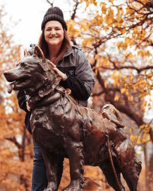 Bronze dog statue displayed in autumn setting with orange leaves in background.