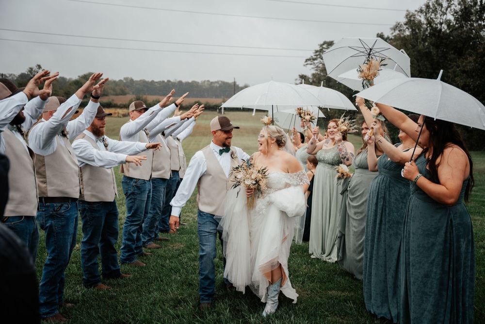 Celebrating couple runs through cheering crowd holding umbrellas at rainy outdoor wedding ceremony.