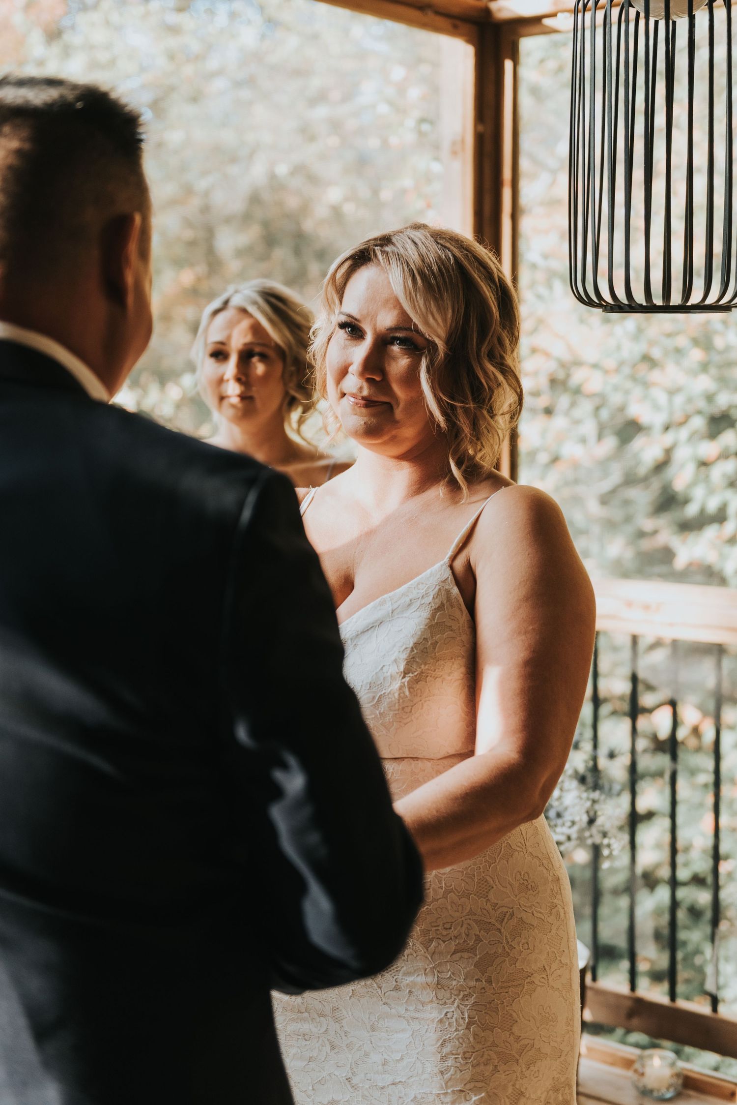 An intimate wedding moment captured on a covered deck with modern pendant lighting and natural scenery.