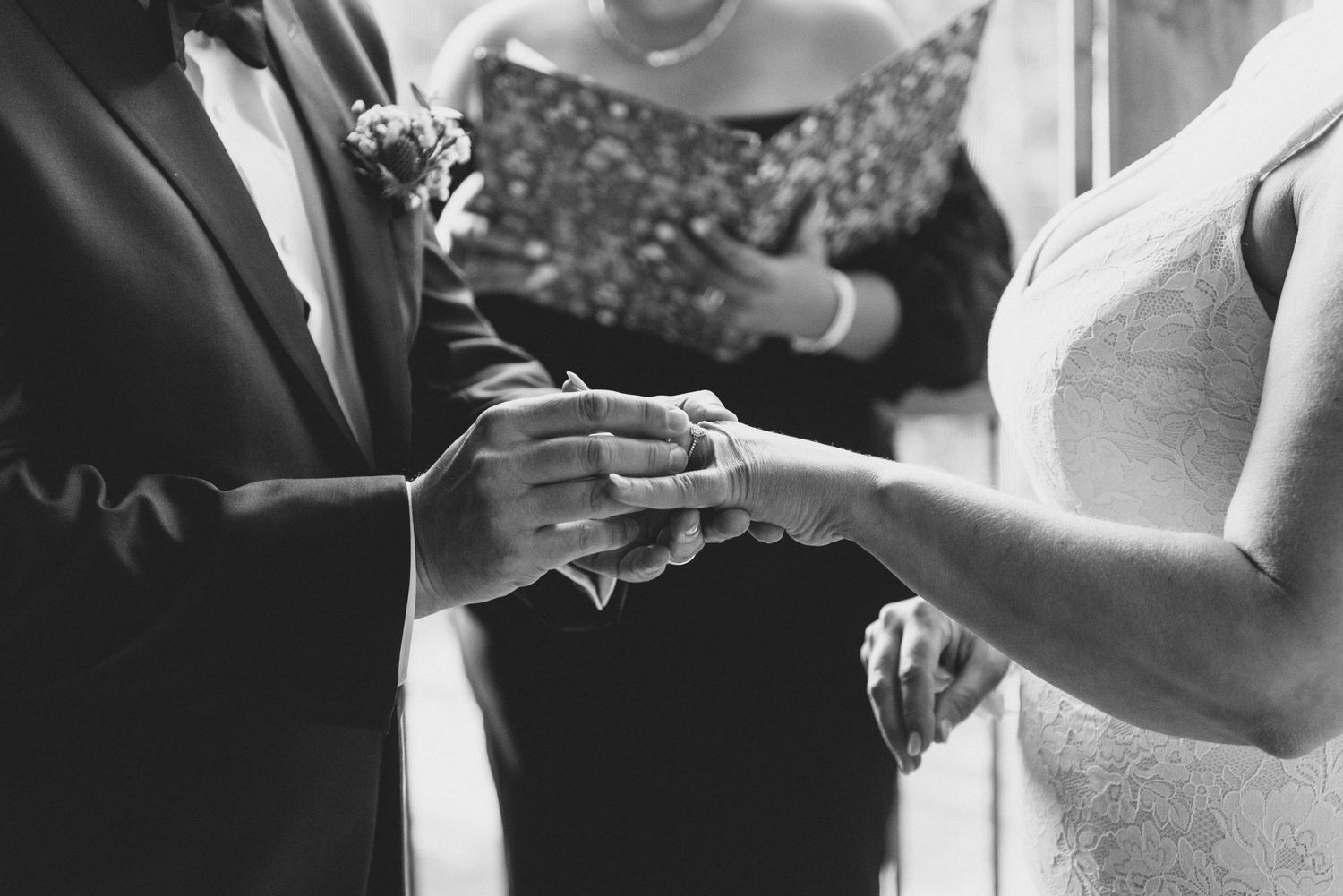 Black and white photo of wedding ceremony ring exchange with close up of hands sharing rings during the vows.