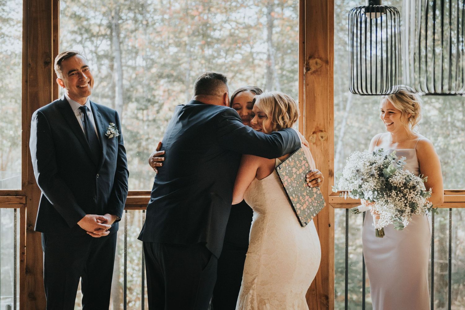 Emotional wedding ceremony moment at rustic wooden venue with a couple embracing while holding white floral bouquet.