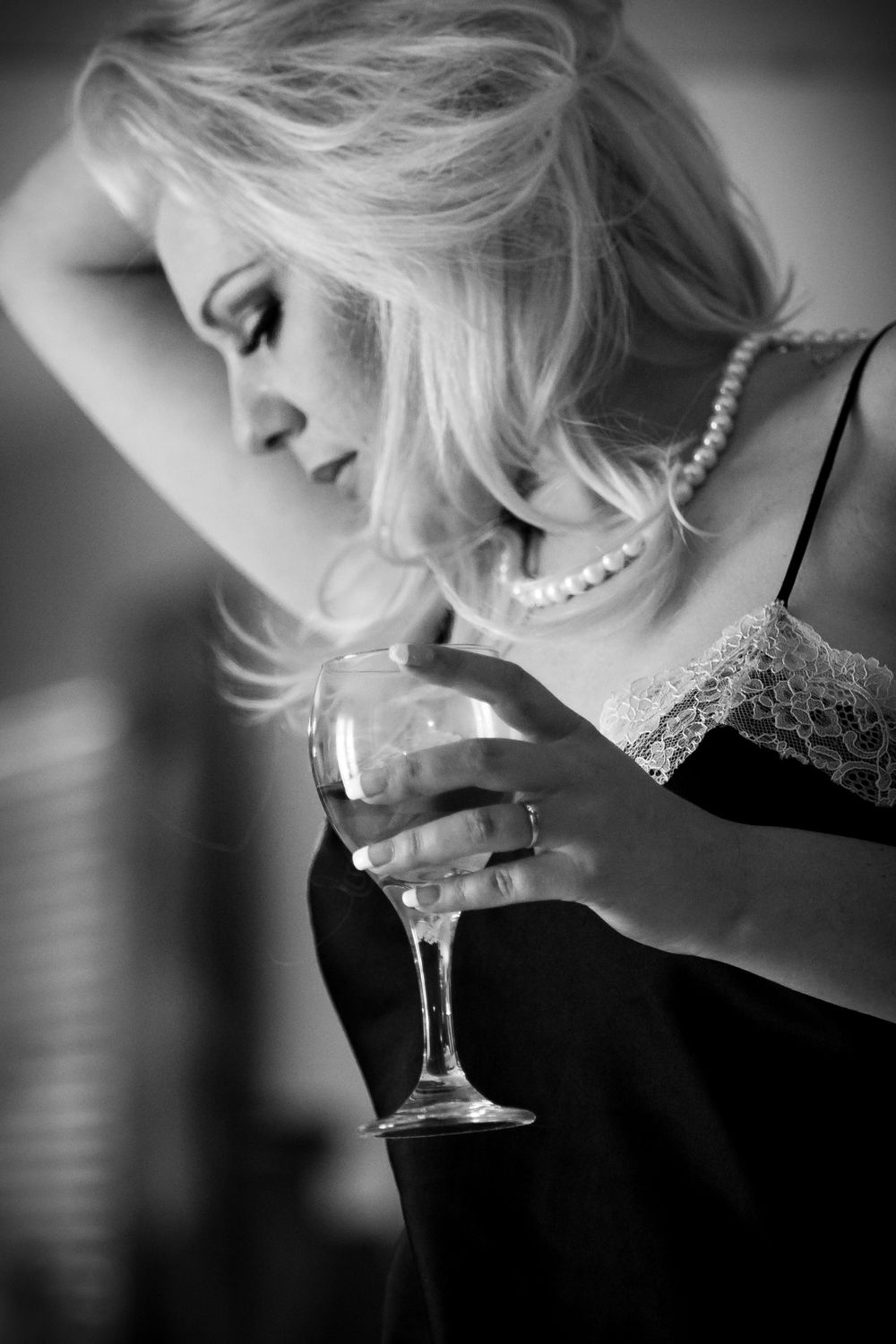 Black and white portrait of a woman in pearls holding a wine glass with dramatic lighting and soft focus.