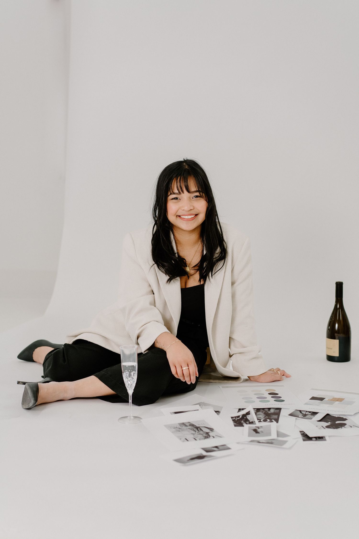 Casual lifestyle portrait with champagne glass and photographs scattered on white studio floor.