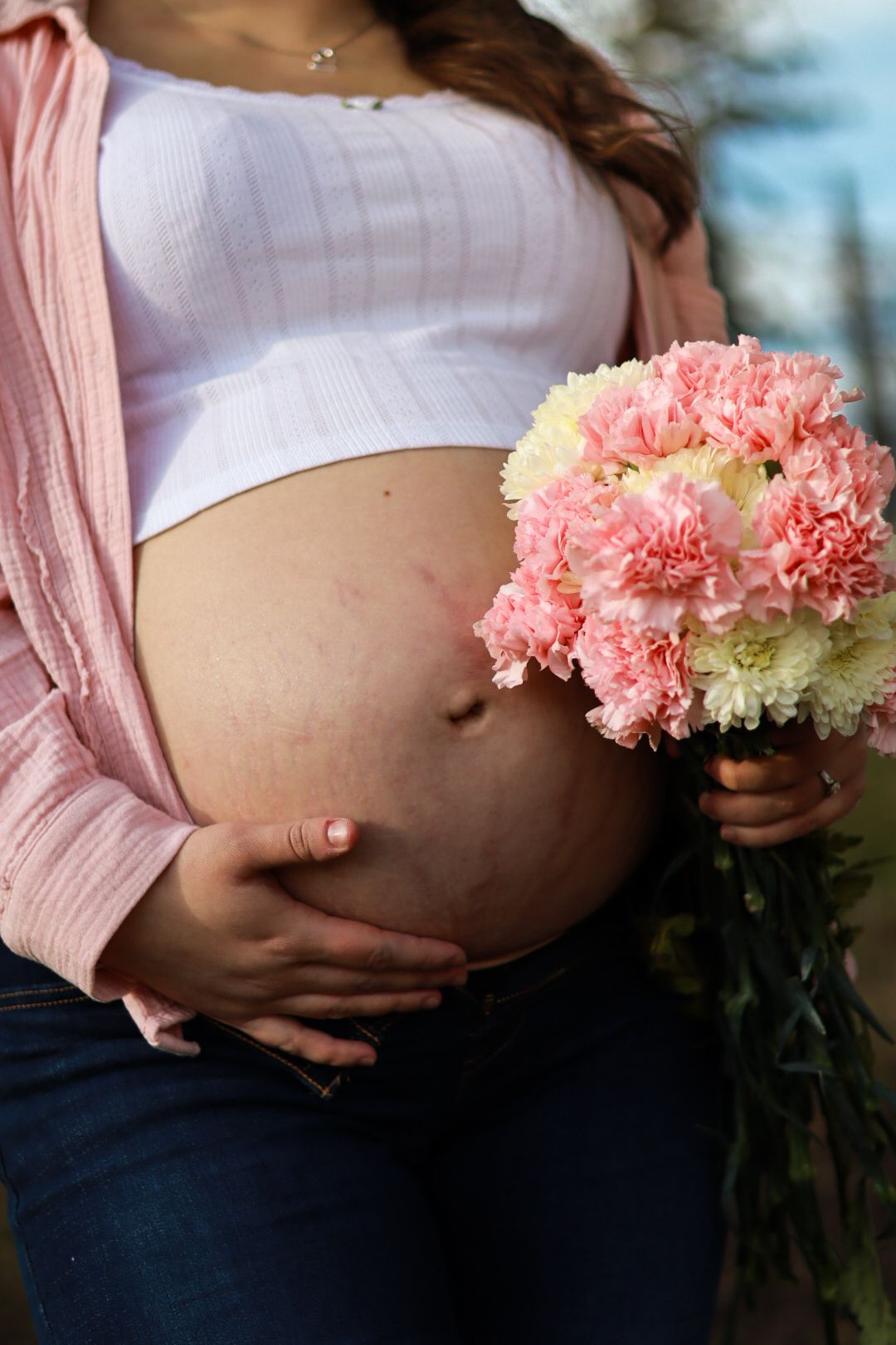 Close-up of pregnant belly with pink carnation bouquet and pink cardigan.