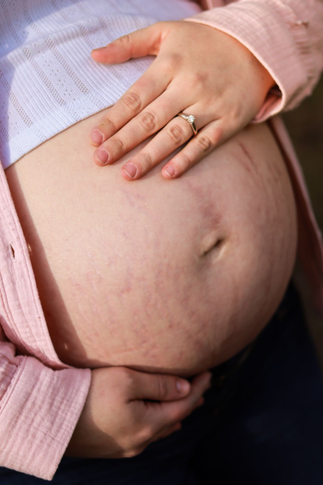 Close-up of pregnant belly with wedding ring visible on hand resting on bump.