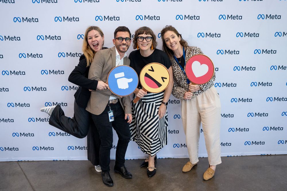Group poses together against a blue and white Meta logo backdrop at a corporate event.