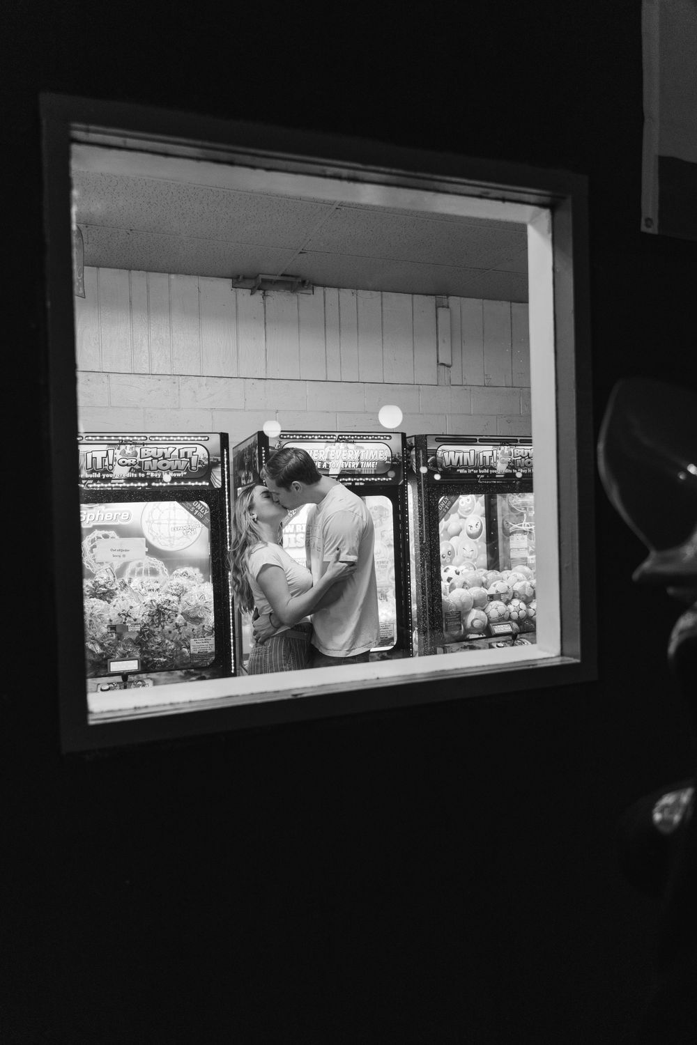 A romantic black and white photograph taken through a window showing a couple embracing in an intimate moment.