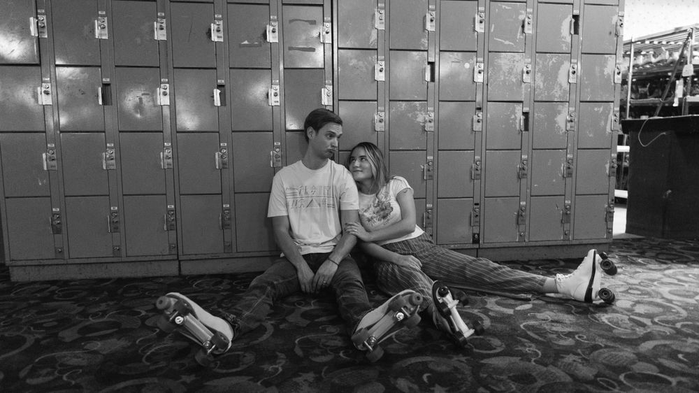 Two people sit together on the ground in front of metal lockers in a black and white photograph.