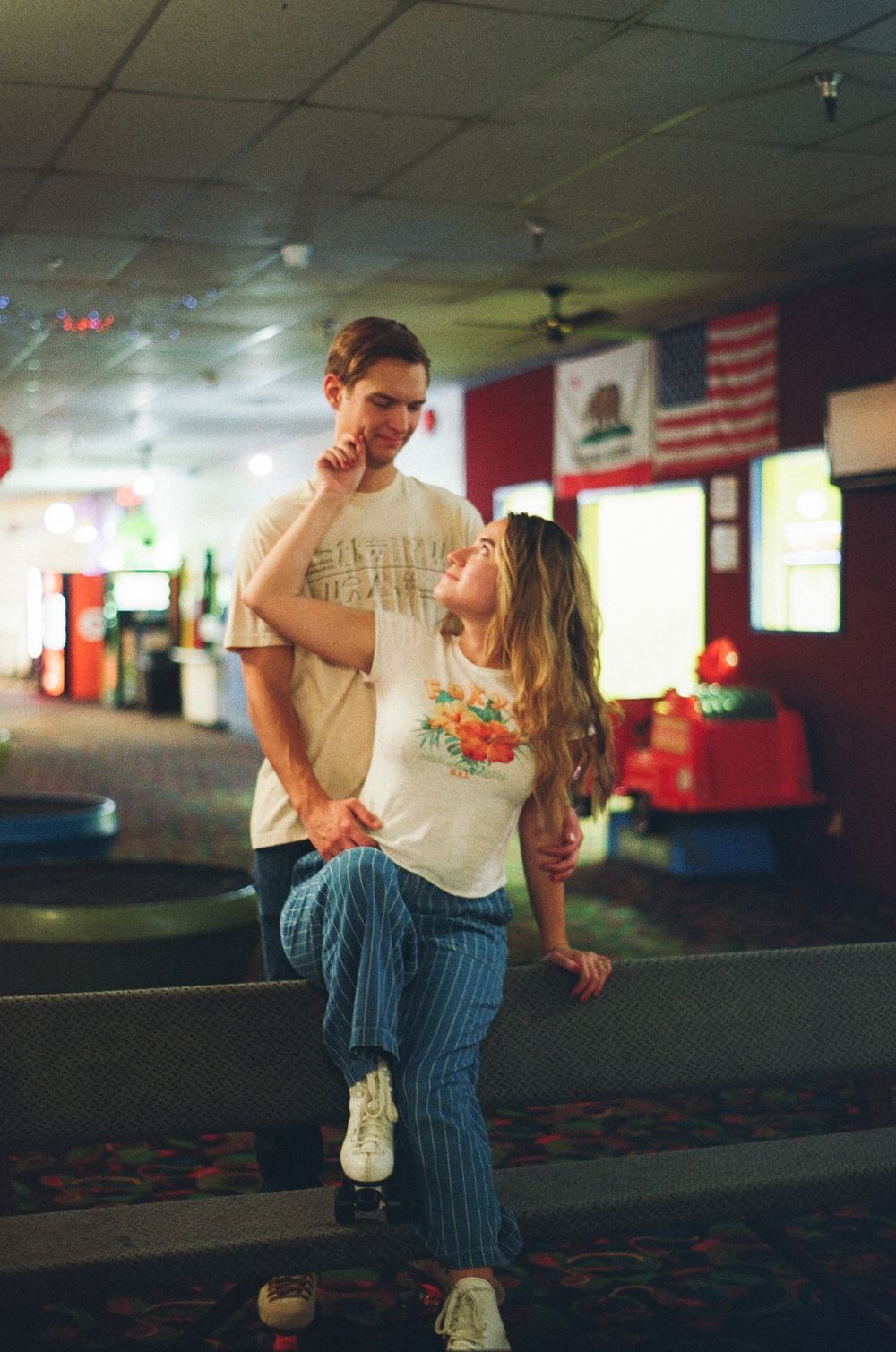A couple shares a romantic moment at a roller skating rink with vintage lighting and decor.