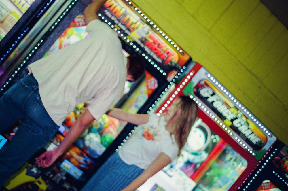 Blurred motion photo in a colorful arcade showing people playing games with neon lights in the background.