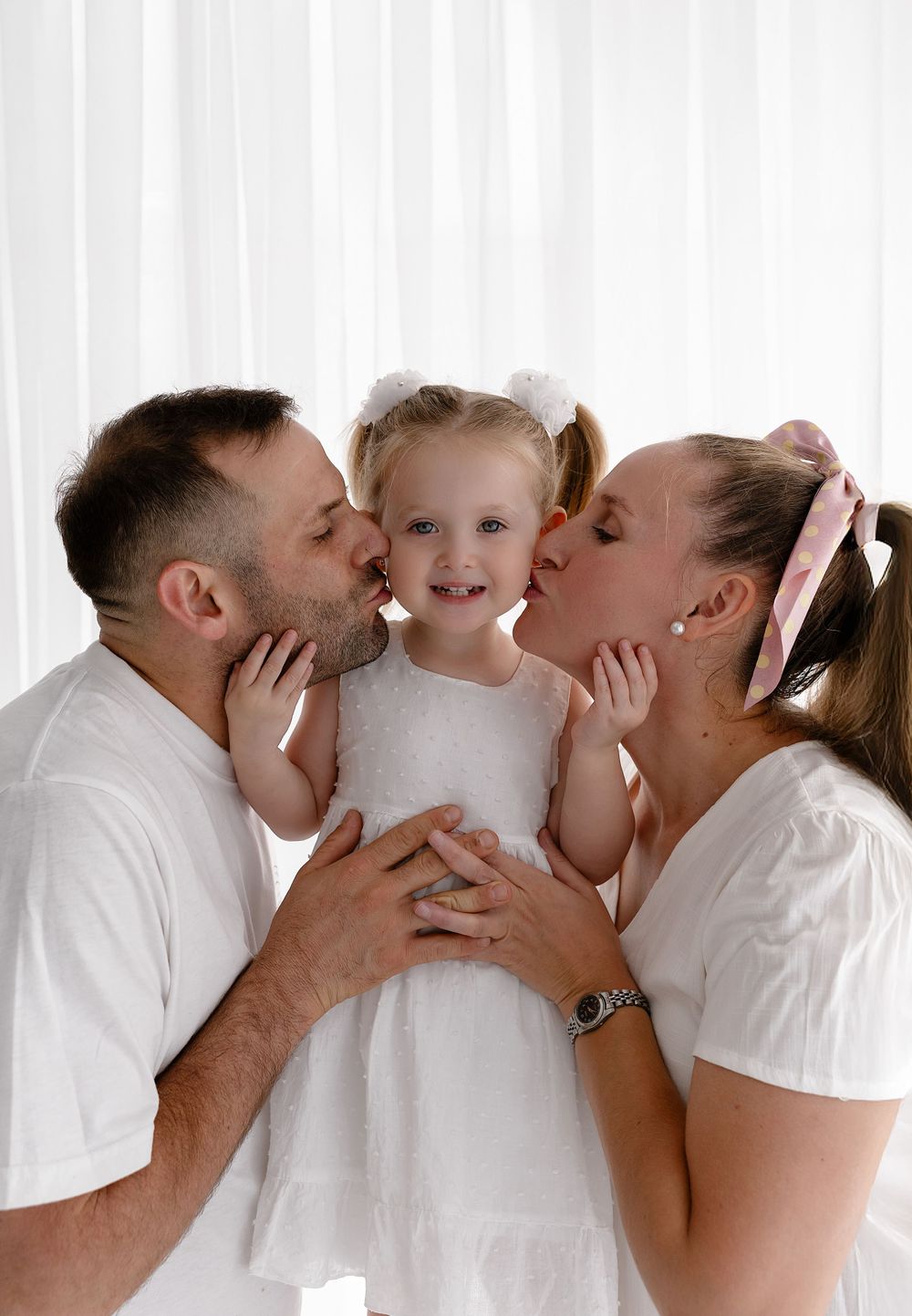 A family in white clothing sharing a tender moment together against a bright background.