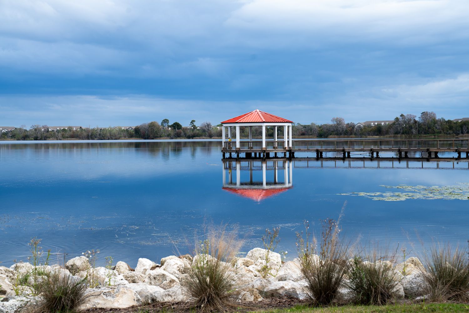 A serene gazebo on a pier overlooking a calm blue lake with cloudy skies.