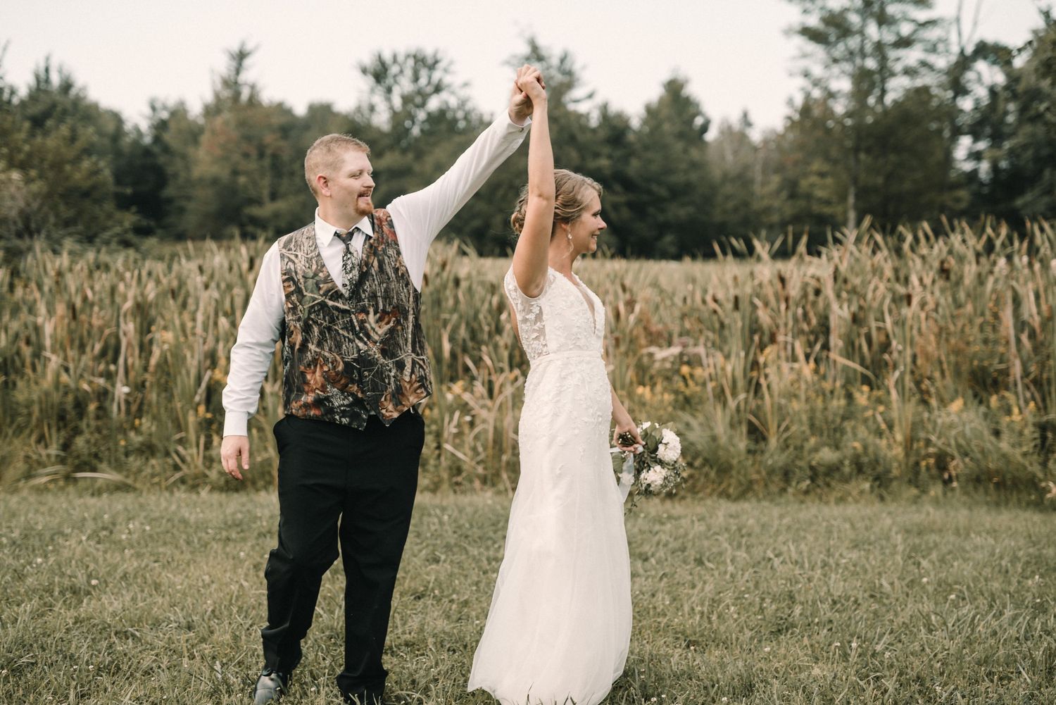 A couple celebrates with raised hands in a field at sunset.