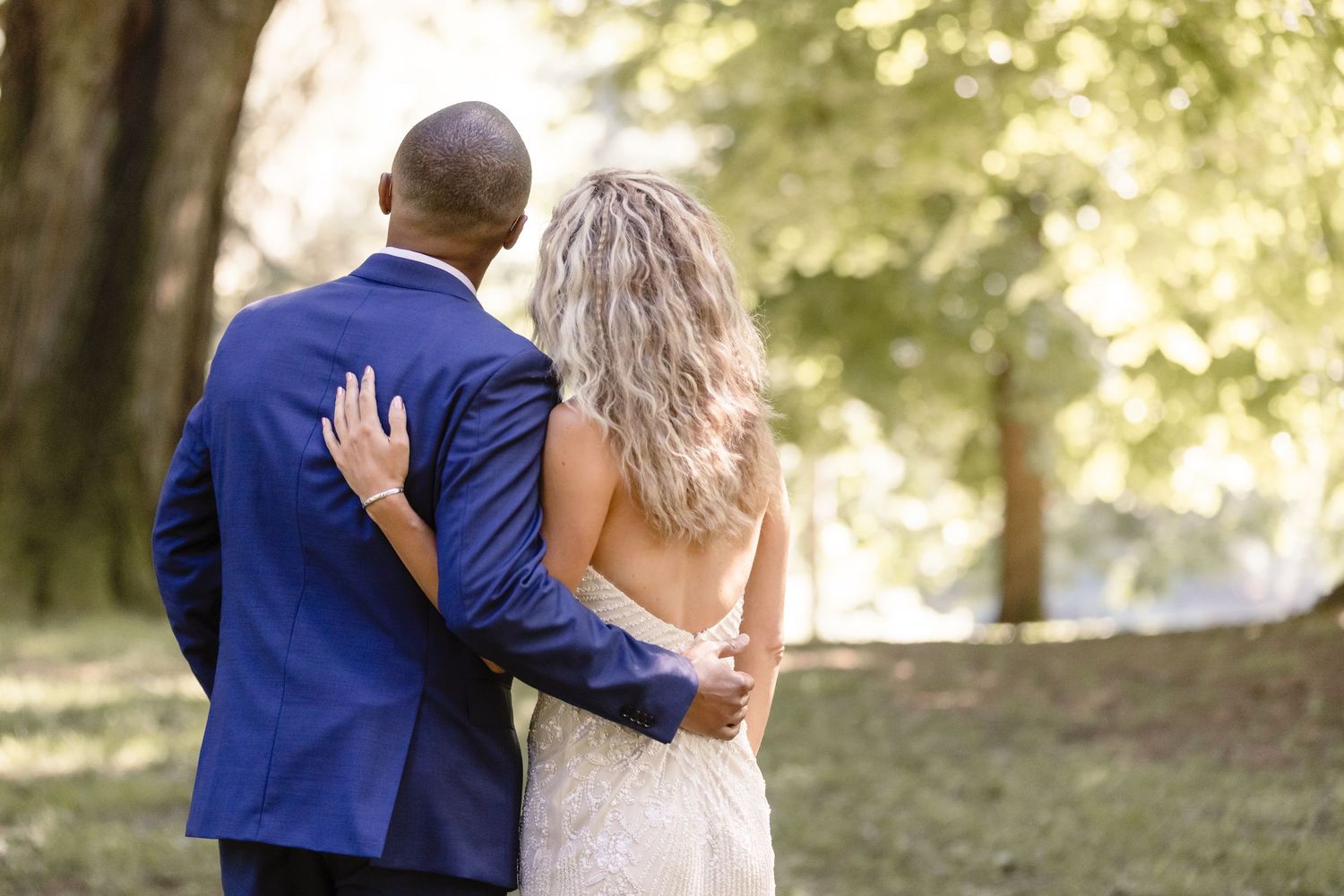 Romantic wedding photo of couple embracing from behind against a natural forest backdrop.