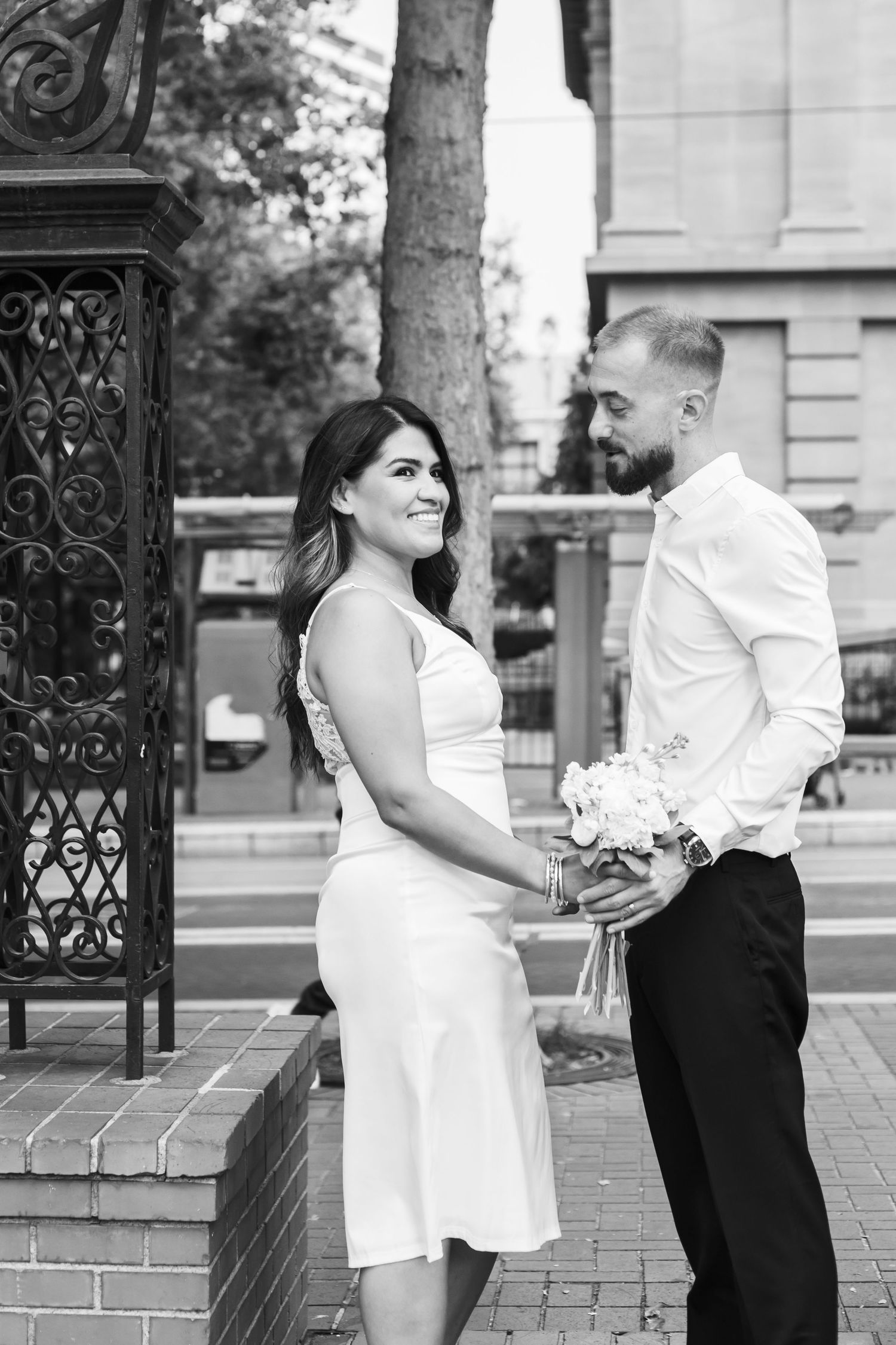 A romantic couple shares tender moments in a series of black and white photos on a brick walkway with ornate iron gates.