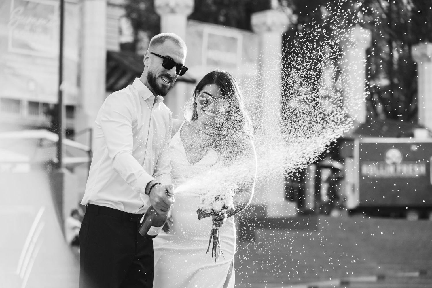 A playful black and white wedding photo with champagne spray and laughter.
