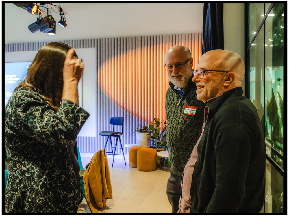 Three attendees engaged in conversation during networking event with orange lighting. Portland event photographer