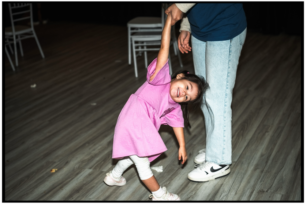 Child in pink shirt dancing and having fun with adult on wooden dance floor. Portland event photographer