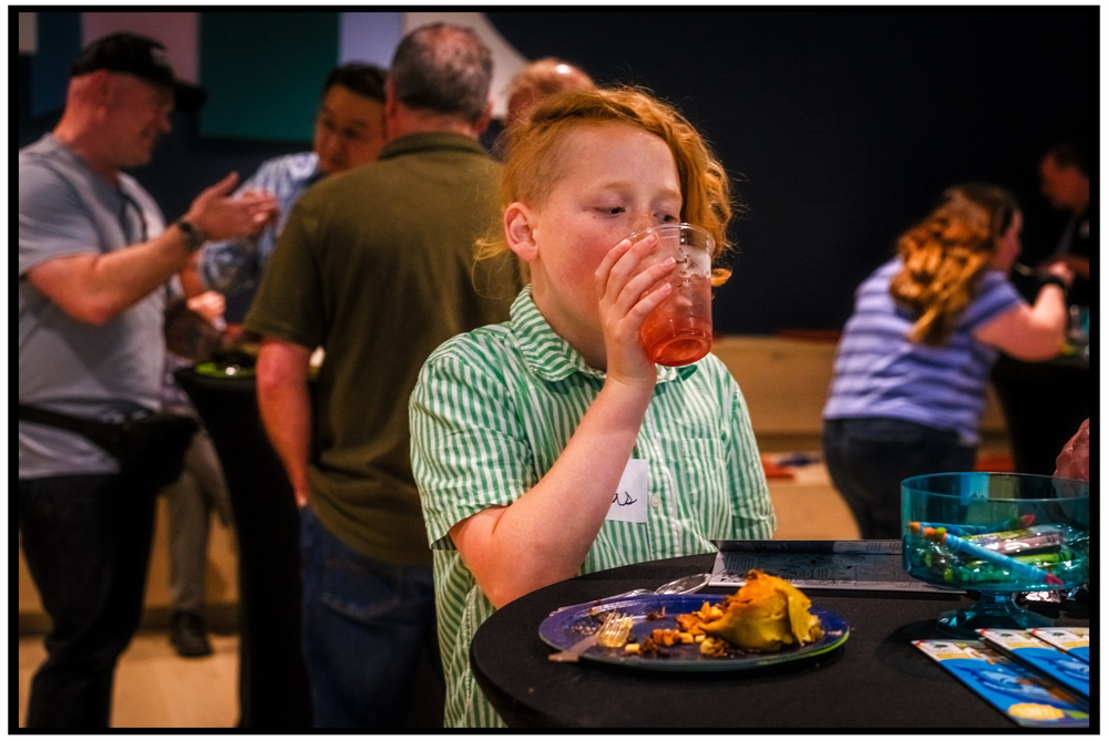 A young person in a striped shirt sits at a table with food looking thoughtful. Portland event photographer