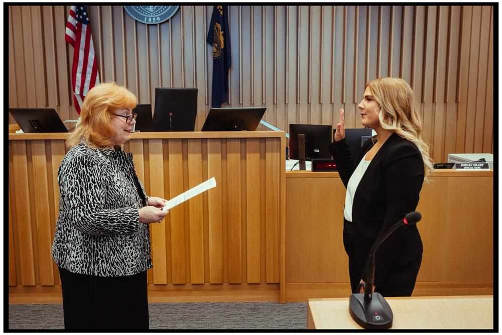 Two people stand in what appears to be a courtroom or government chamber with an American flag visible. Portland event photographer