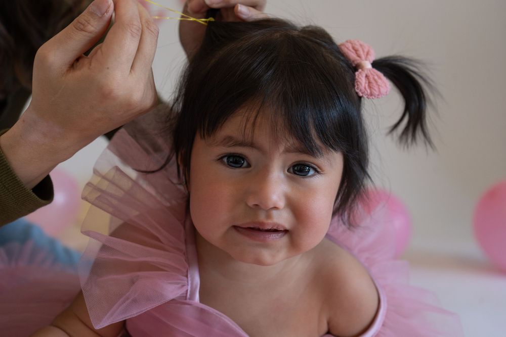 A small child in pink clothing smiles while being styled with hair accessories.