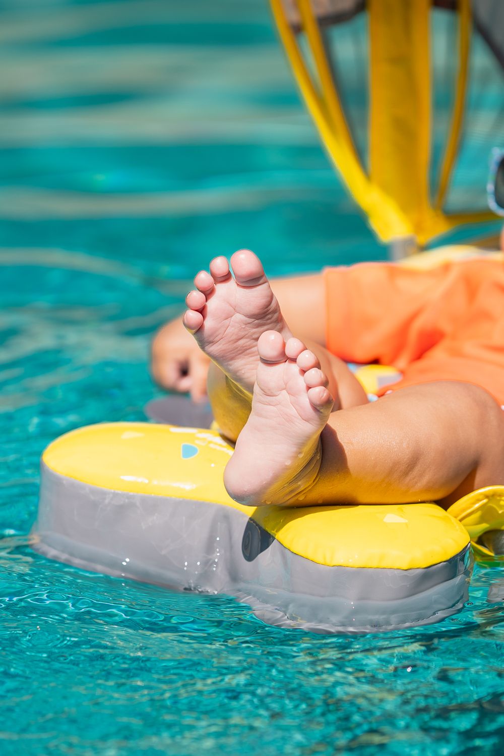 Small feet resting on yellow pool float in bright turquoise water.