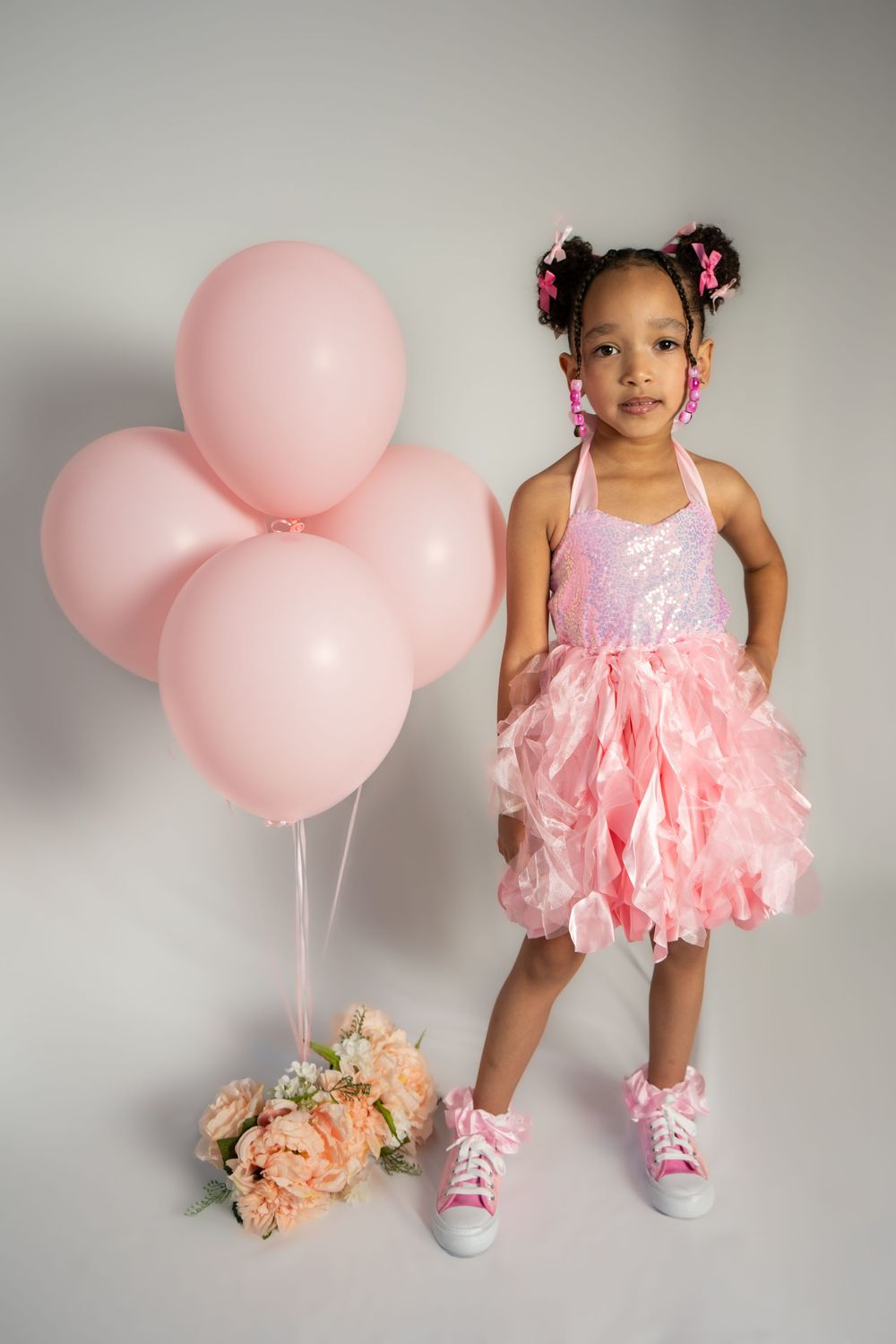Pink tutu dress and balloons set up for a birthday photoshoot on grey background.