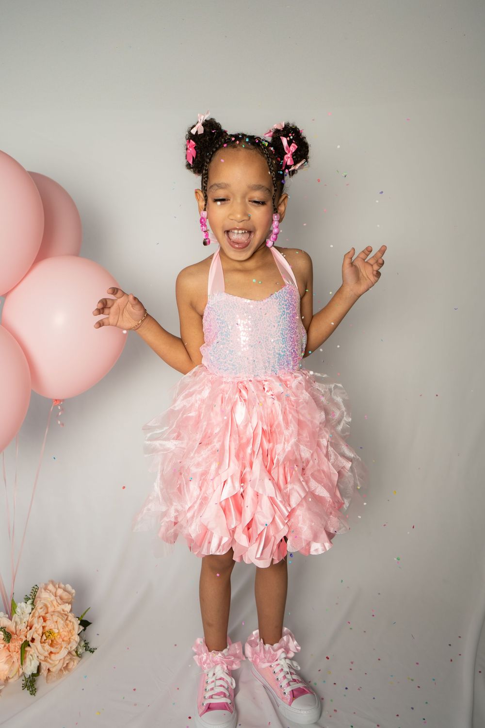 Joyful dance poses with pink balloons and tutu dress against grey backdrop.