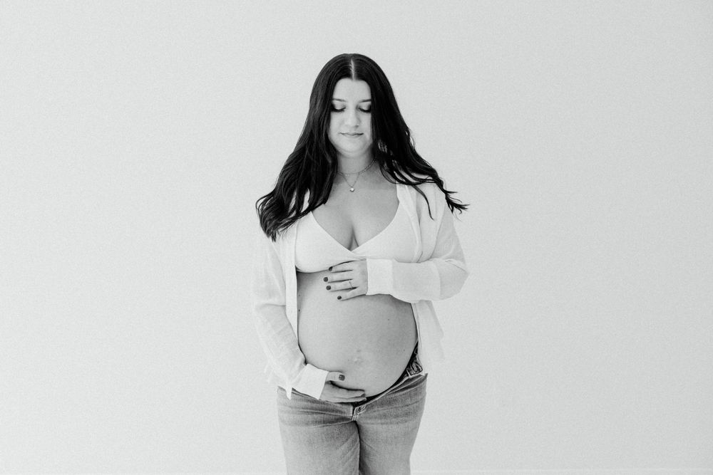 Minimalist maternity portrait of an expectant mother in white against a light background.
