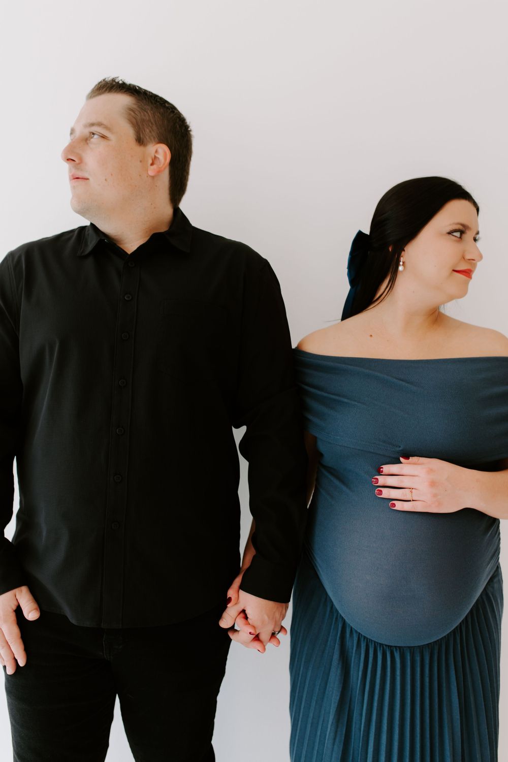 Formal maternity portrait with couple in black and blue attire against white backdrop.