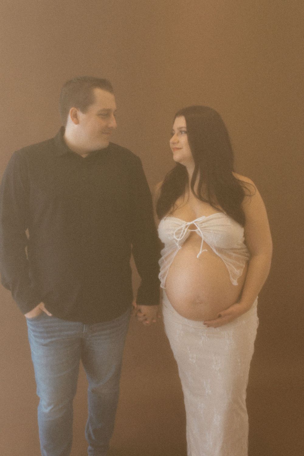 Warm-toned maternity portrait with couple in casual and formal wear.